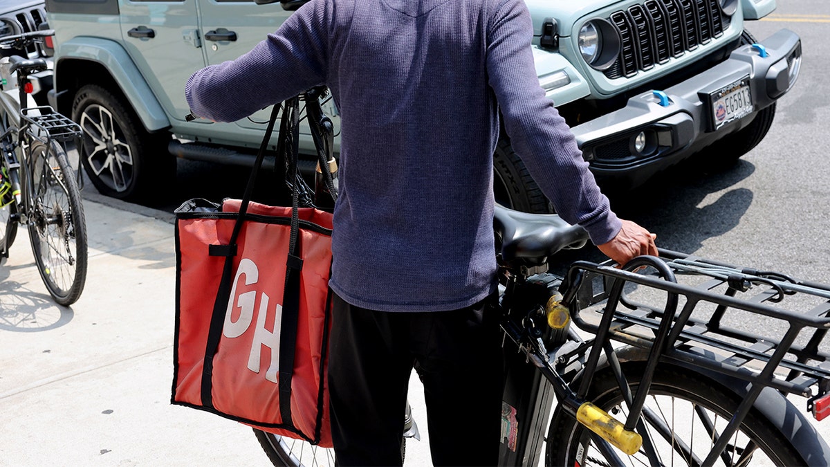 Um homem está na frente de uma bicicleta com uma bolsa GrubHub.