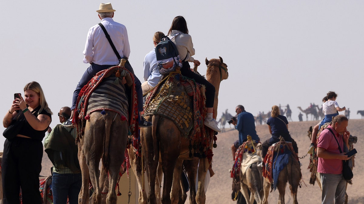 tourists on camels visit the Giza pyramid complex