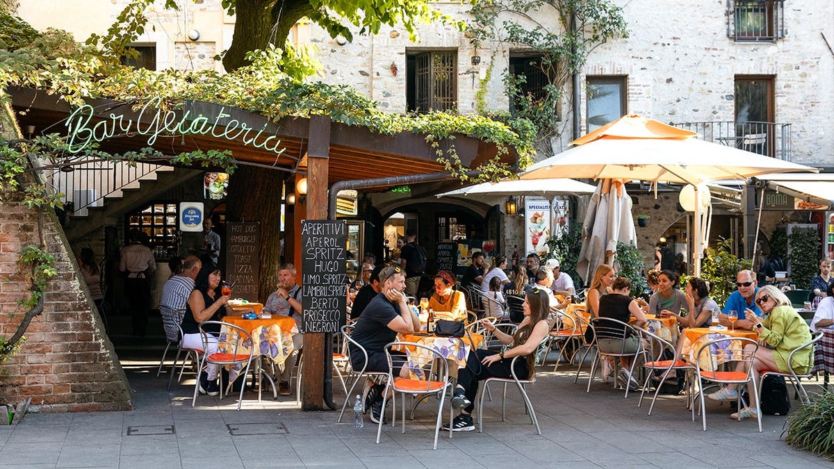 People enjoying aperitivo at an outdoor gelateria shaded by trees in Sirmione, Italy