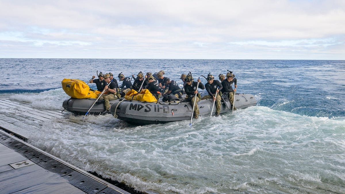 U.S. Navy divers prepare to deploy from USS John P. Murtha in small boats at sea