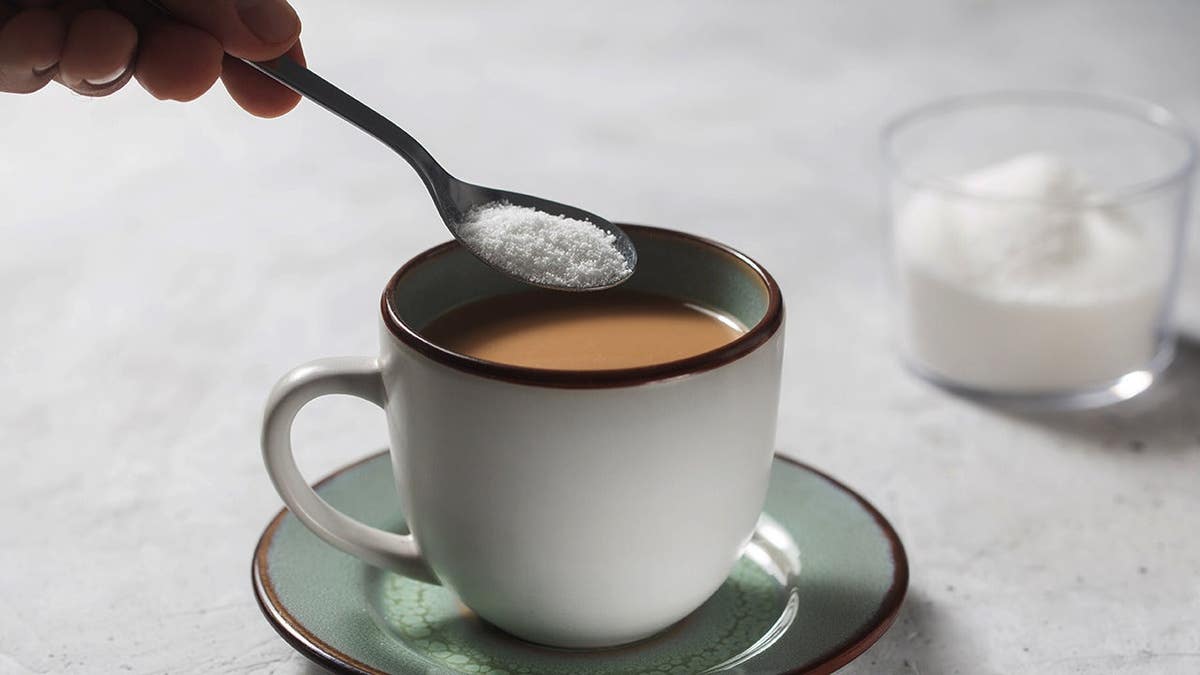 hand pouring spoonful of artificial sweetener into coffee mug.