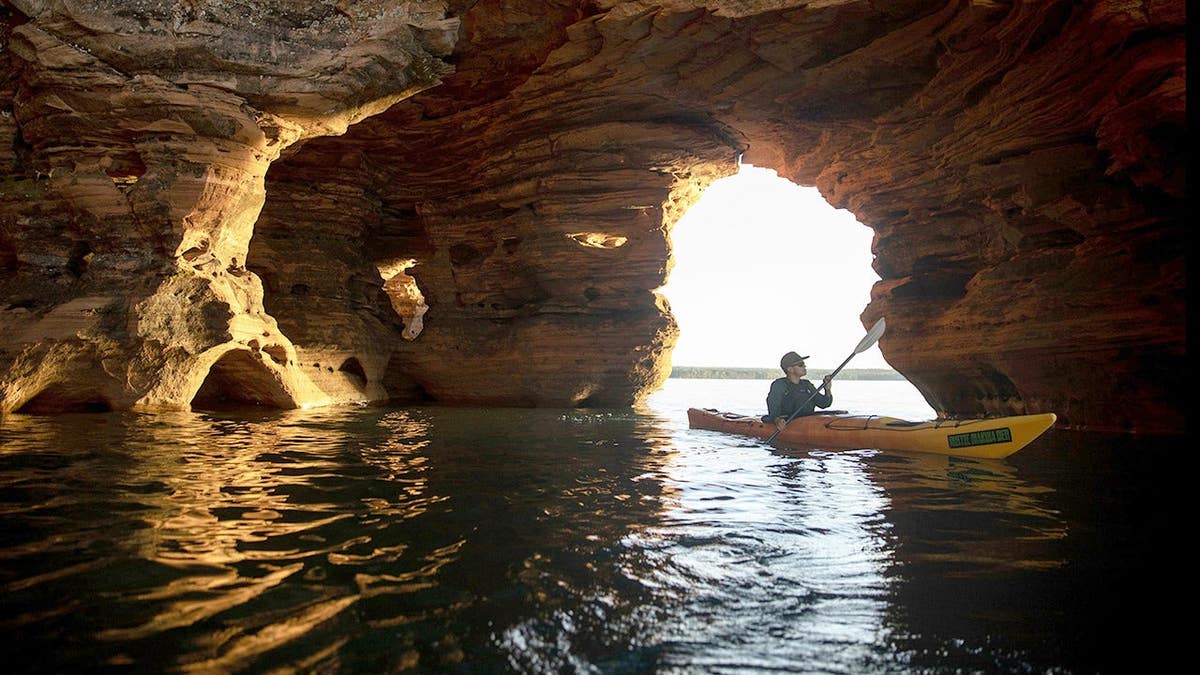Homem andando de caiaque pelas cavernas marítimas da Península de Bayfield na Área Natural Estadual das Falésias Marítimas das Ilhas Apóstolo, em Wisconsin.