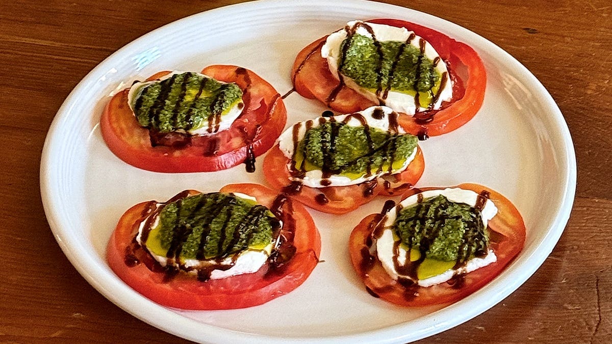 A close-up of bruschetta with Besto on it, topped with diced tomatoes and herbs on a plate.