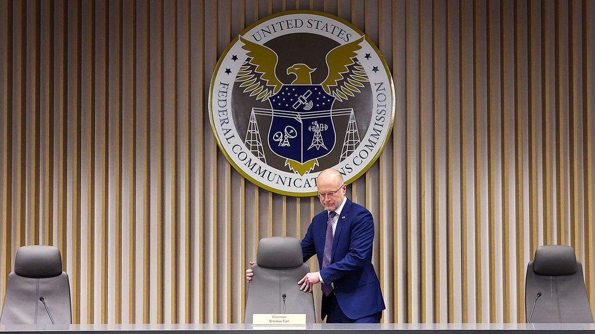 FCC Chair Brendan Carr takes a seat in front of the department's emblem.
