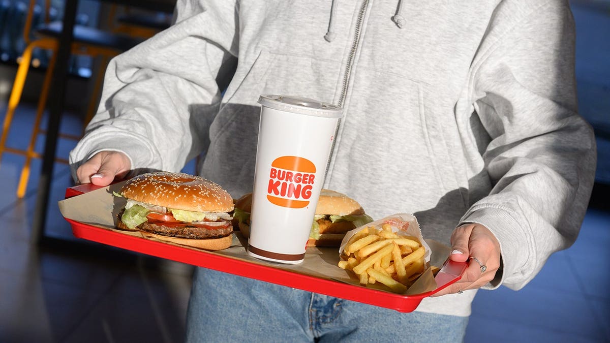 A woman carrying a tray with plant-based burgers, nuggets, fries, and a Coke inside a Burger King restaurant.