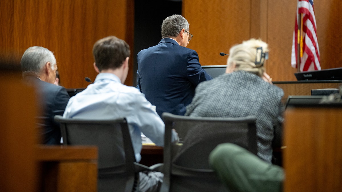 Tyler Robinson and Kathryn Nester sitting at a table with their backs to the camera in a courtroom setting.