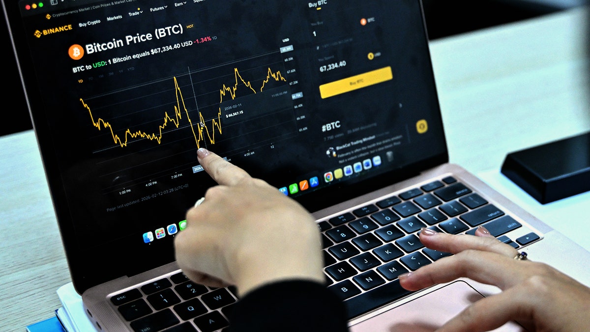 A woman points to a bitcoin price chart on a laptop.