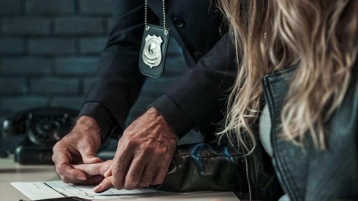 Detective taking fingerprints from arrested woman in interrogation room