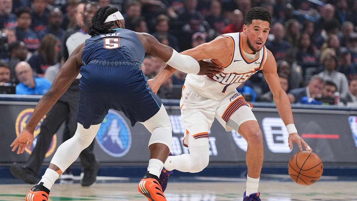 Phoenix Suns guard Devin Booker driving past Oklahoma City Thunder guard Luguentz Dort during a basketball game.