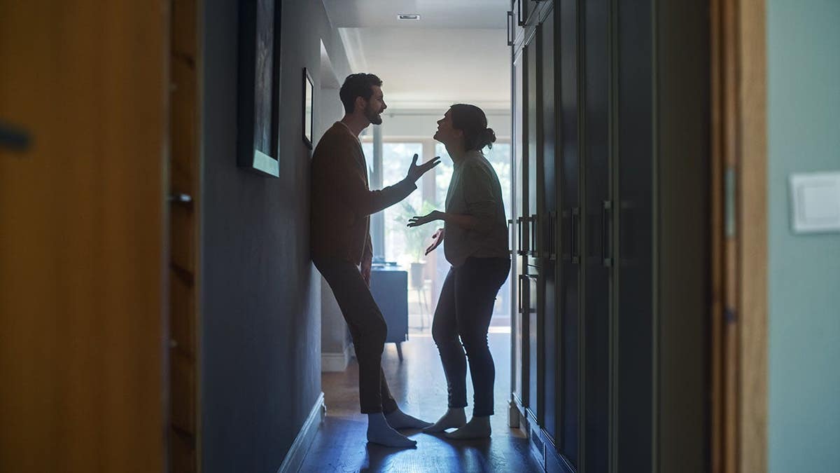 A young woman and man arguing in a dark apartment hallway