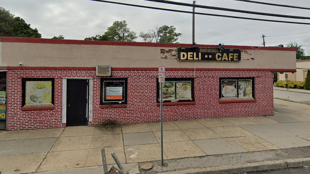 The deli is in the corner of a commercial building with red bricks and a black door. Small windows are blocked out with images of menu items.