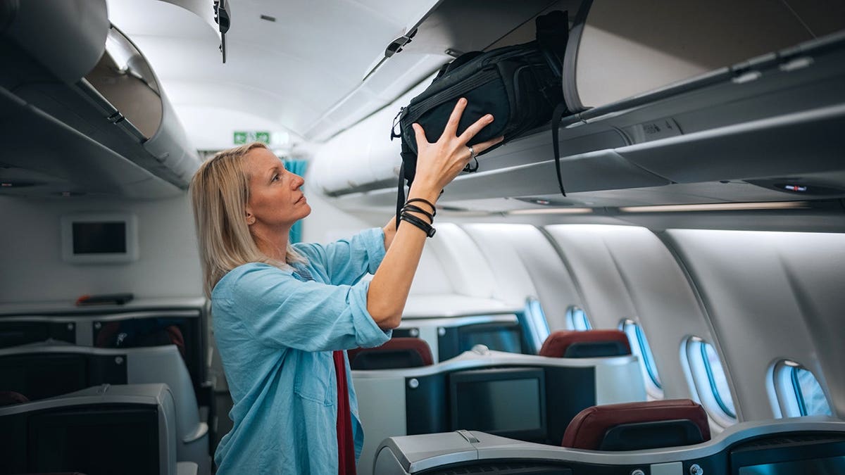 Female passenger placing luggage in overhead locker inside airplane business class cabin
