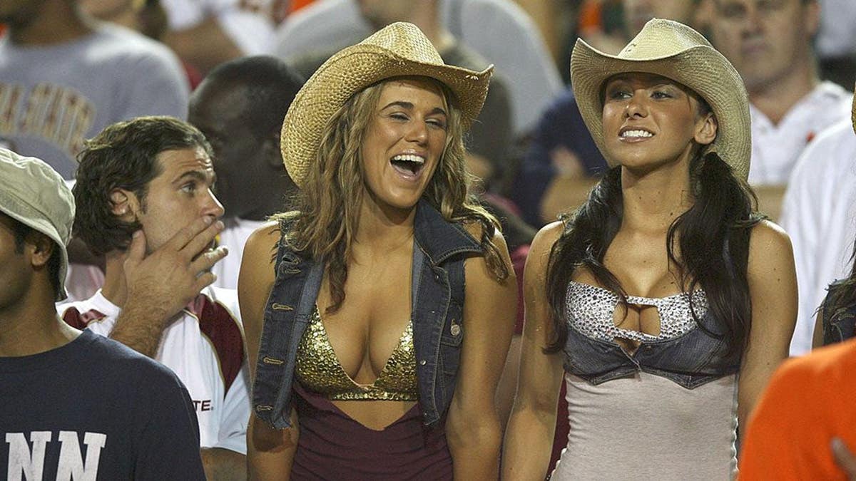 FSU Cowgirls Fabiola Romero e Jenn Sterger sentadas em arquibancadas em jogo de futebol