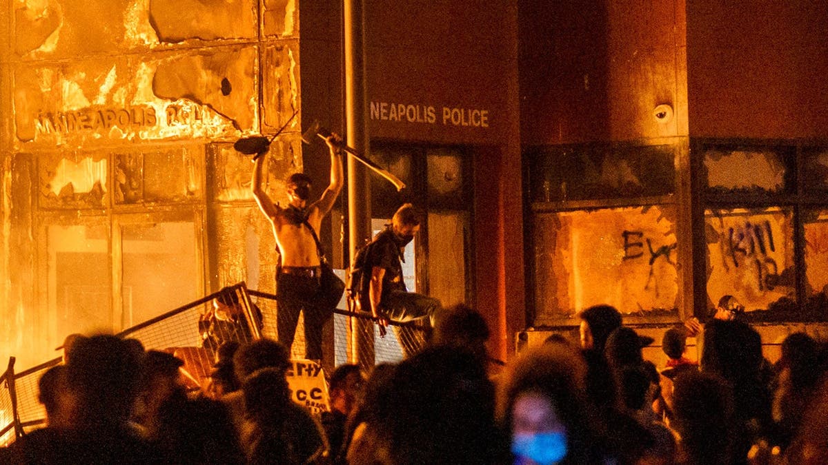 Protesters stand on barricade as flames engulf police precinct building.