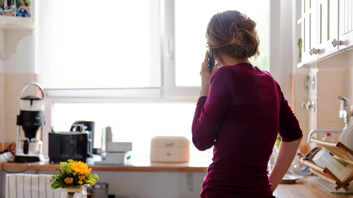 A woman takes a phone call in a kitchen.