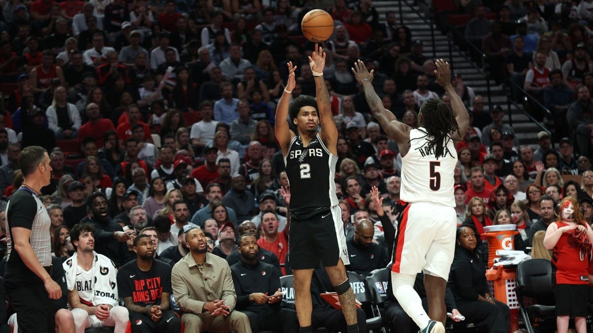 San Antonio Spurs combo guard Dylan Harper shoots a 3-pointer over Portland Trail Blazers PG Jrue Holiday at Moda Center.