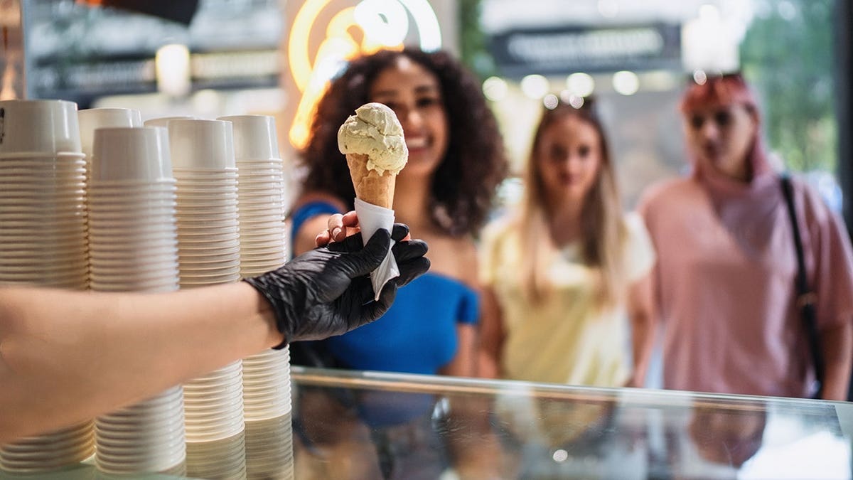 Ice cream shop worker wearing black gloves serving an ice cream cone to customers