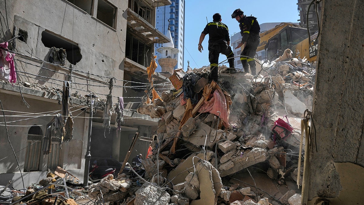 Lebanese civil defense workers walk across a large mound of concrete rubble and debris.