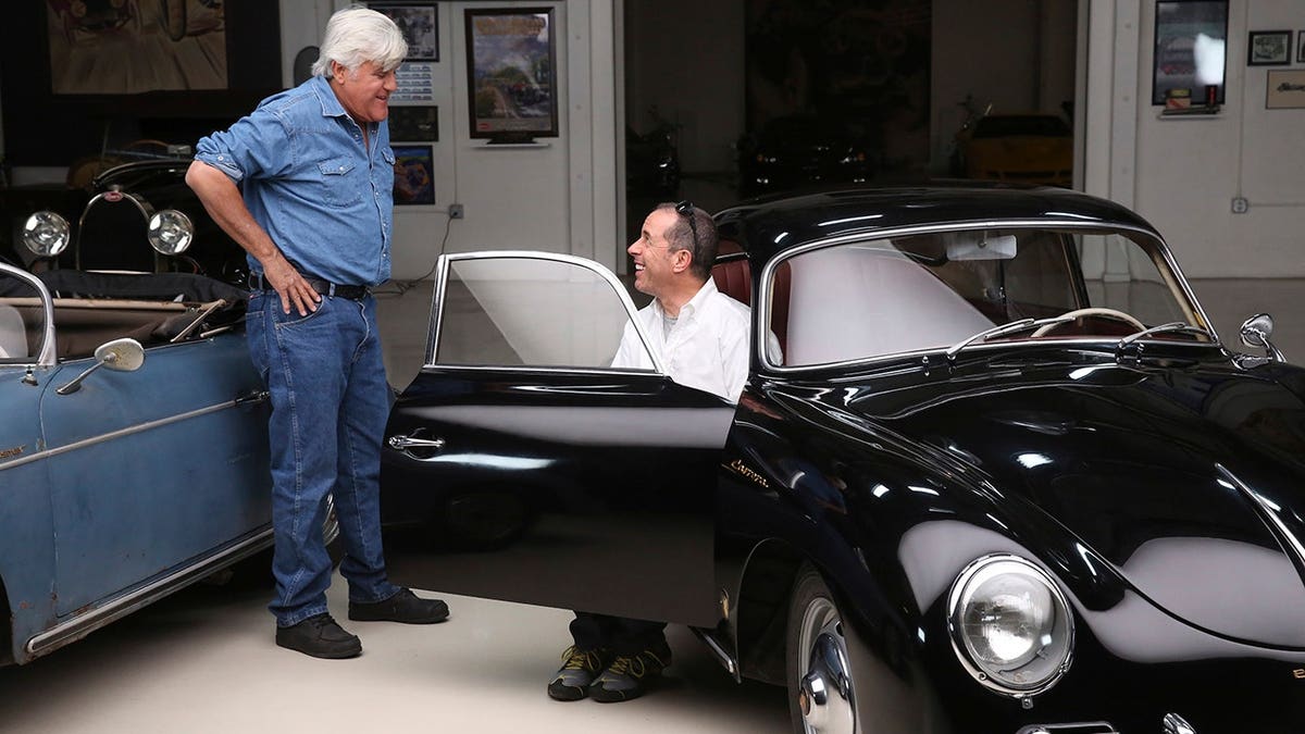 Jerry Seinfeld and Jay Leno standing together in a garage with classic cars