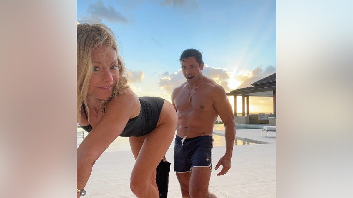Kelly Ripa and Michael Consuelos posing in their swimsuits by the pool.