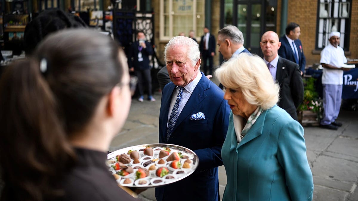 King Charles III and Queen Camilla looking at a platter of fruits and chocolates at Covent Garden market