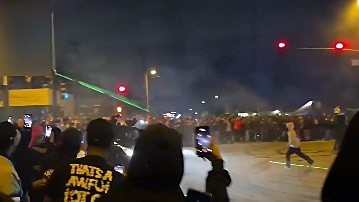 Onlookers record a car doing donuts in an intersection.