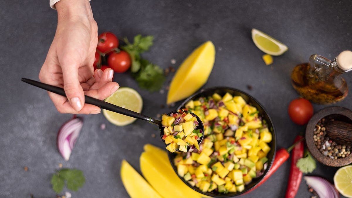 Freshly made mango salsa in a black ceramic bowl on a table with ingredients