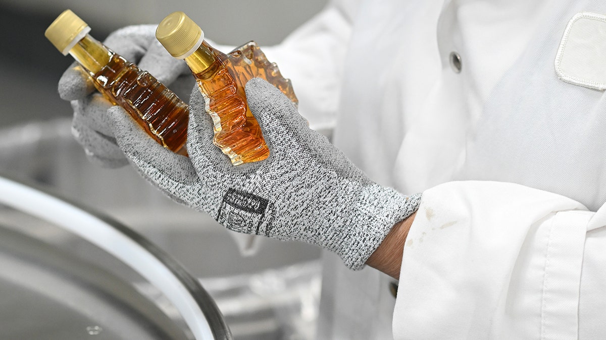 Um trabalhador retira garrafas de xarope de bordo da linha de engarrafamento em uma instalação de Turkey Hill em Granby, Quebec, Canadá, na segunda-feira, 23 de março de 2026. A empresa fornece produtos de bordo direcionados aos mercados de presentes, souvenirs e viagens.