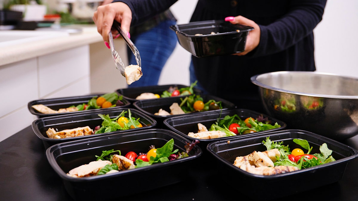A woman using a kitchen scale to portion ingredients for a healthy meal