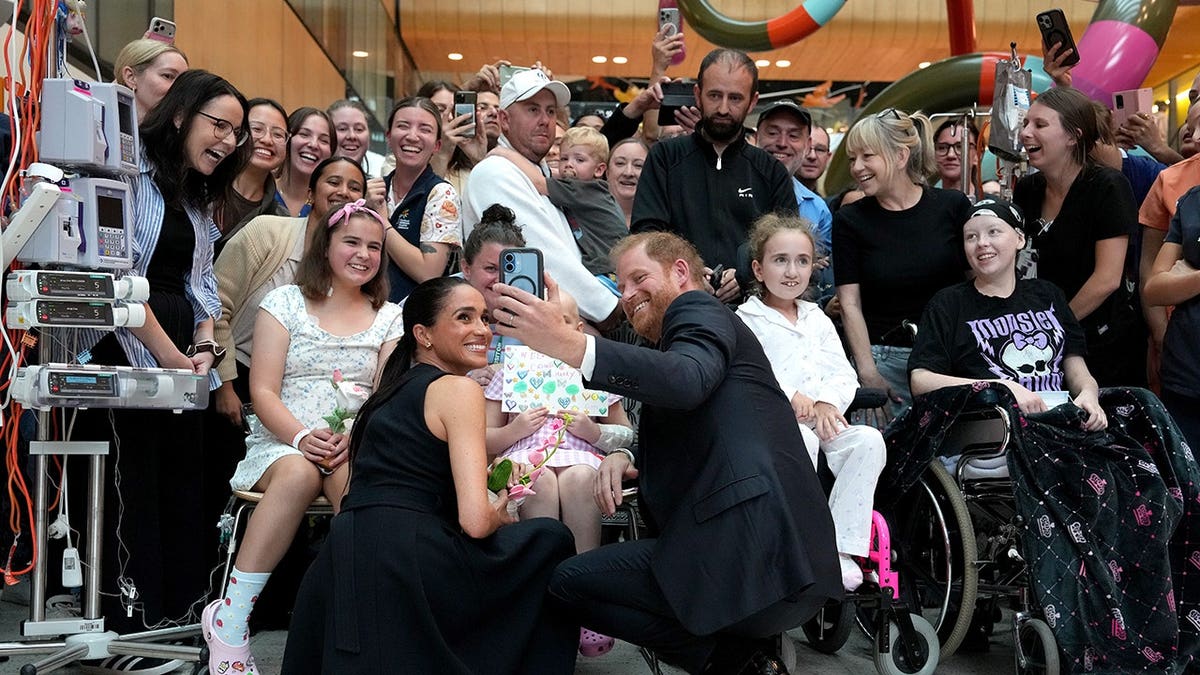 Meghan Duchess of Sussex and Prince Harry Duke of Sussex posing for a selfie with children and families at a hospital