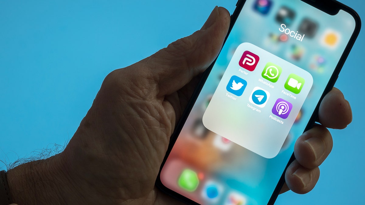Uma pessoa segura um smartphone com aplicativos de mensagens à mostra.