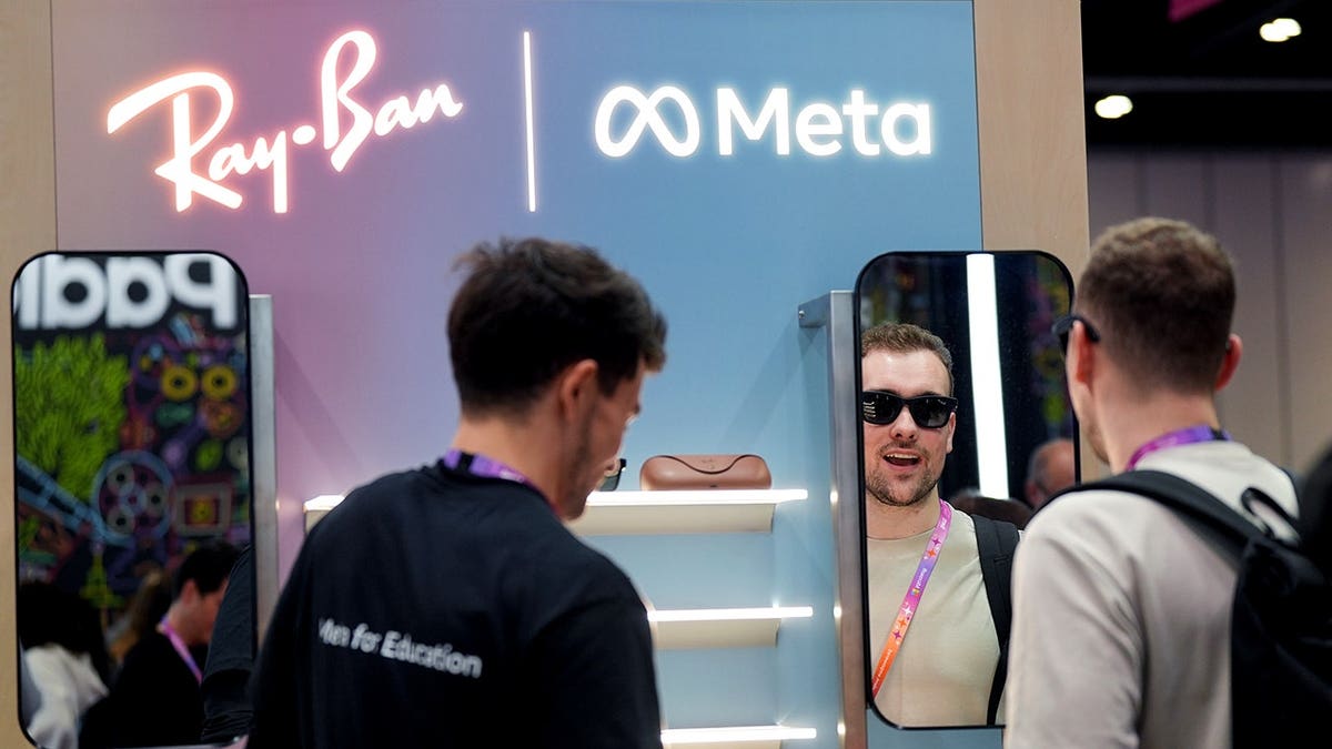 A man looks into a mirror while wearing sunglasses at an exhibit with Ray-Ban and Meta branding.