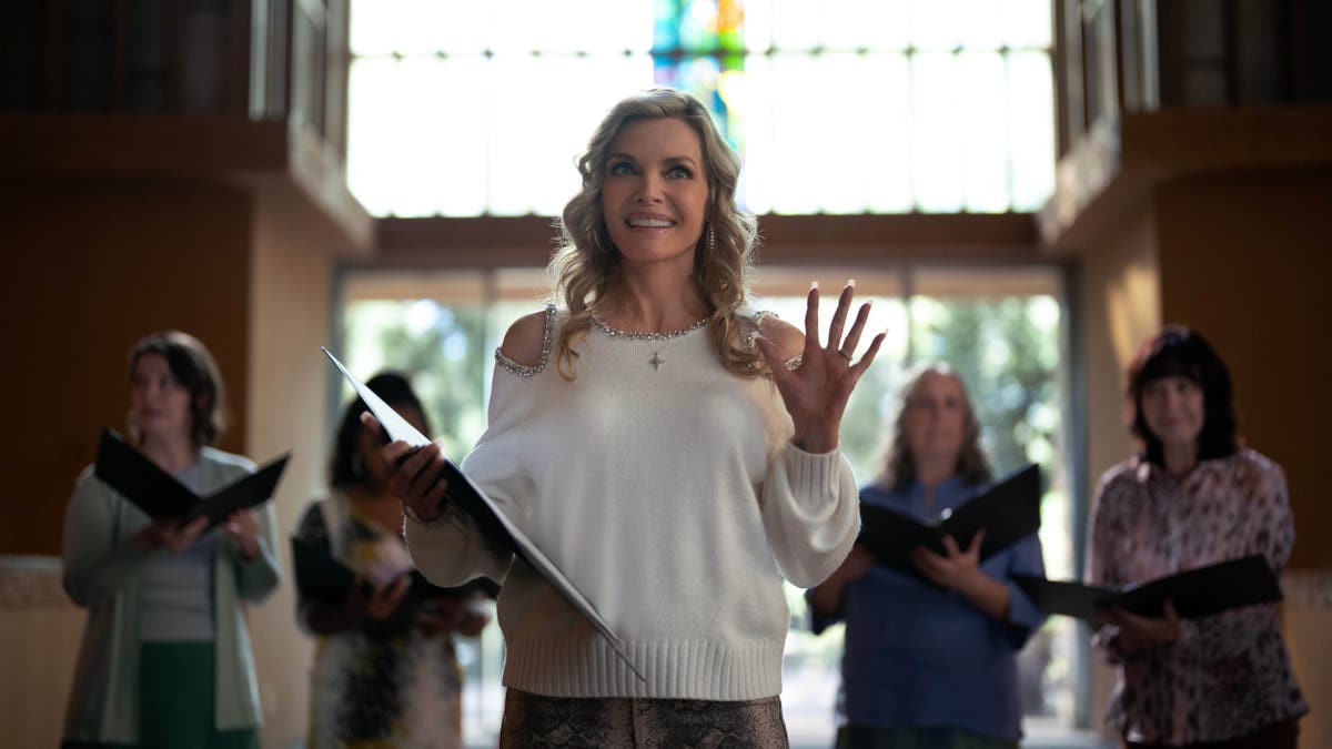 Michelle Pfeiffer holding her hand up in a church in Margo's Got Money Troubles