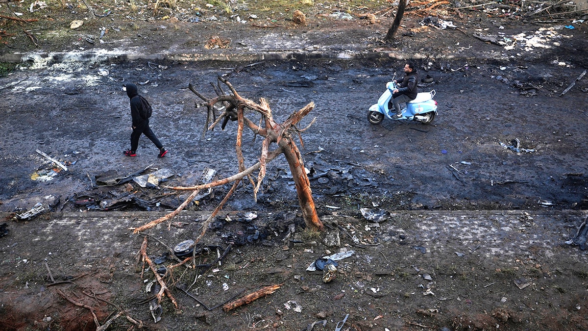 A man rides a scooter past a burned tree and charred debris in Beirut