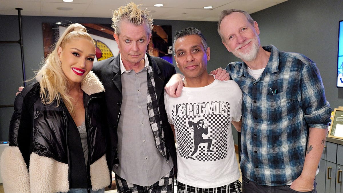 Gwen Stefani, Adrian Young, Tony Kanal, and Tom Dumont of No Doubt standing together at a concert venue.