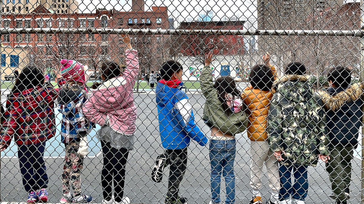 Students line up along a chain link fence.