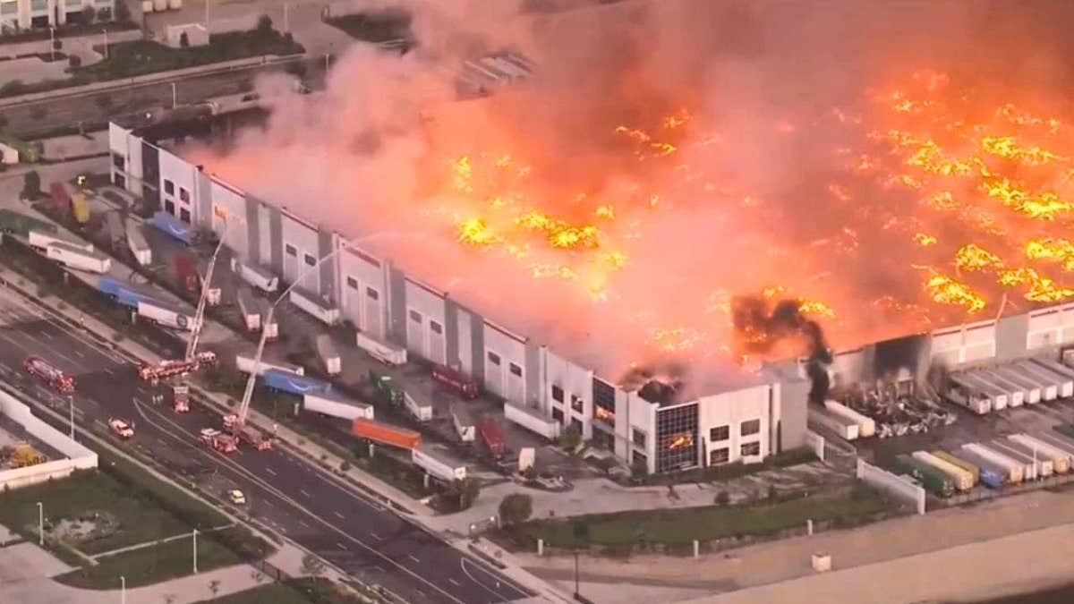 Aerial daytime representation  of a ample  warehouse connected  occurrence  with flames and dense  smoke, arsenic  firefighters respond   from the ground.