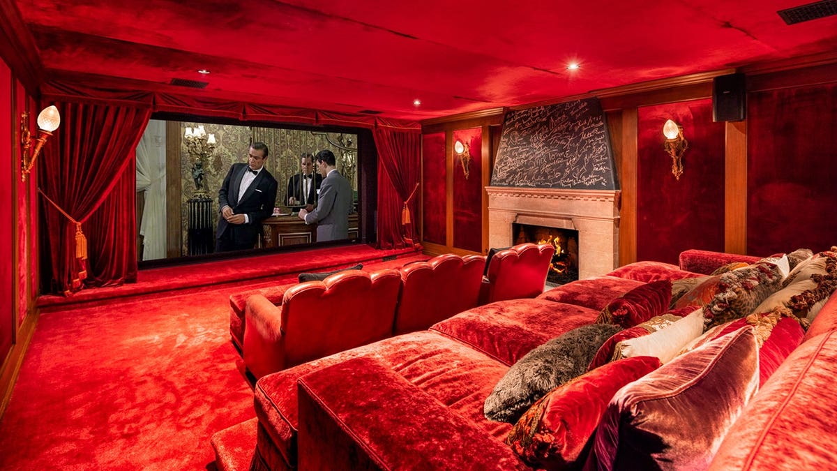 A theater room with red velvet seats and a fireplace.