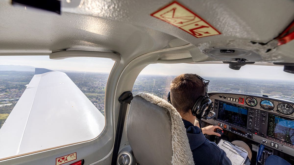 Pilot wearing headset flying light aircraft over mountainous terrain seen through cockpit window