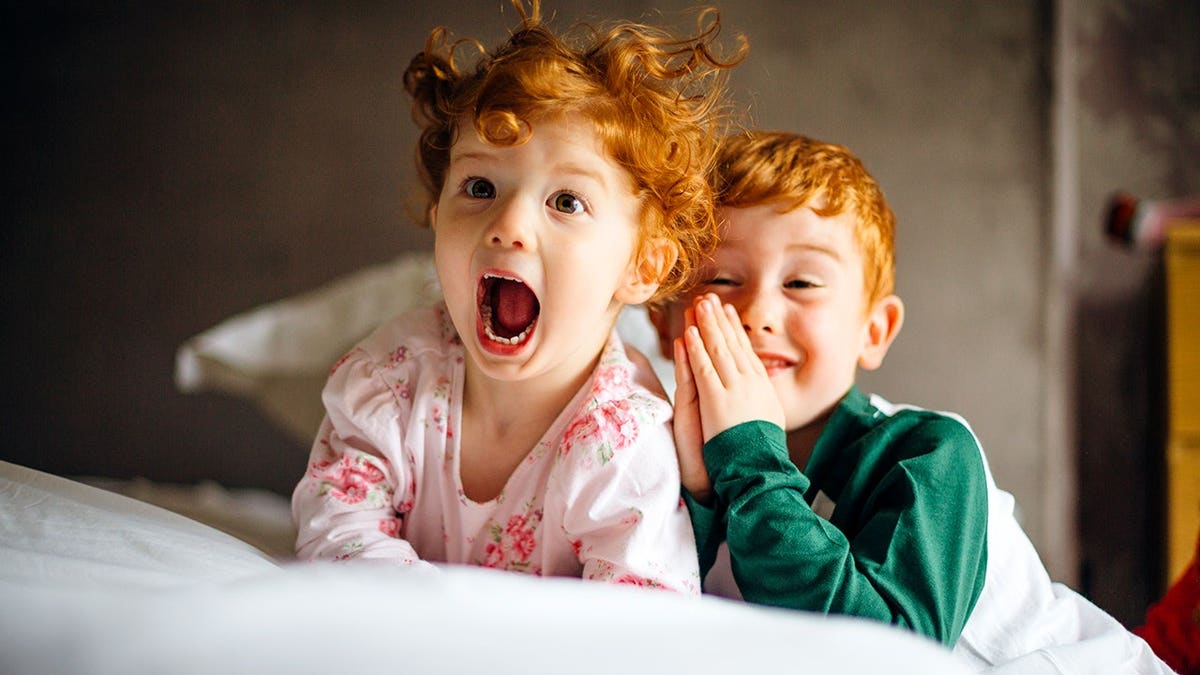 Little girl and older brother in pajamas sitting on bed