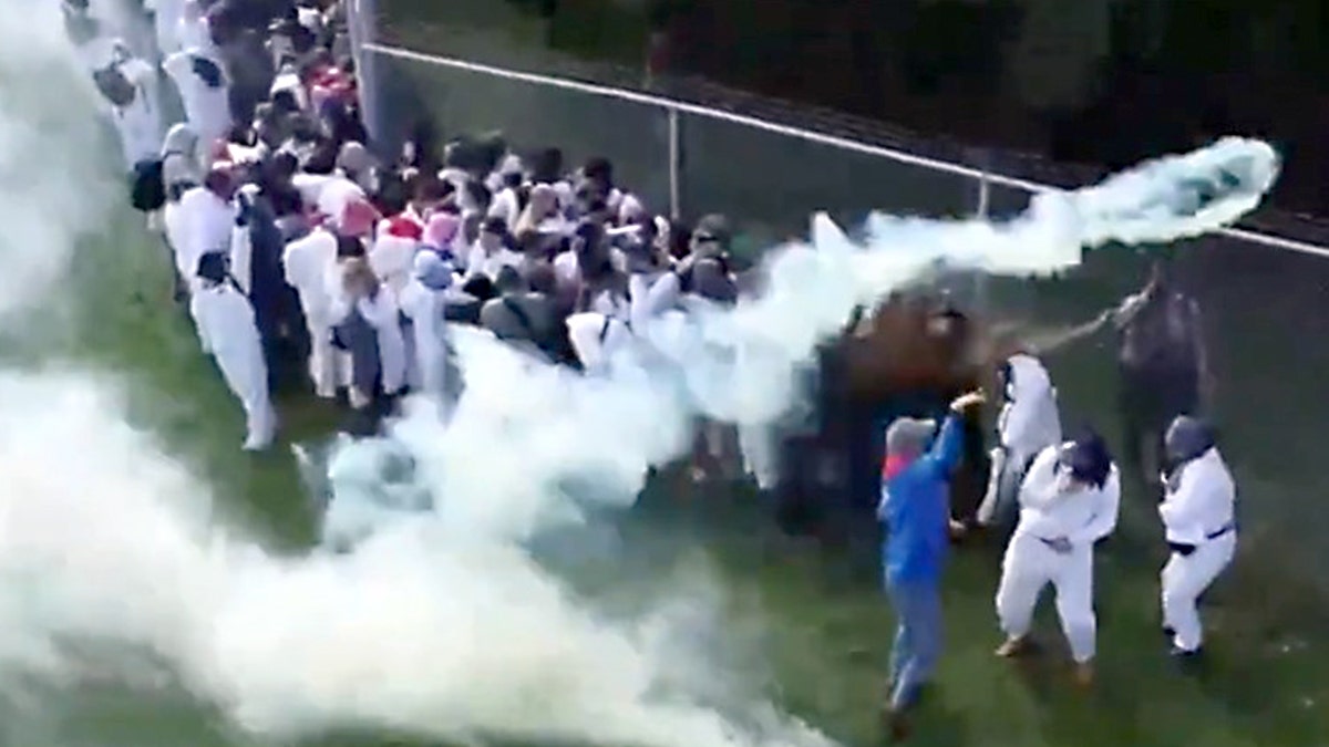 Protesters line a fence, throwing smoking canisters over the fence.