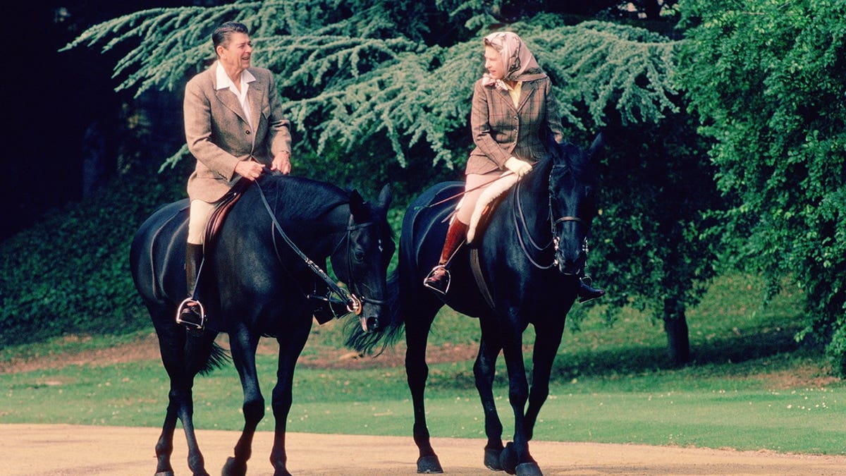 US President Ronald Reagan and Queen Elizabeth II riding horses outdoors.