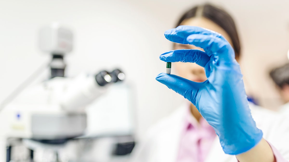 scientist in a lab holds up a blue and white pill