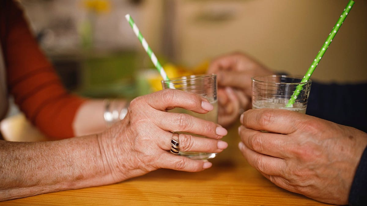 Senior couple holding hands across a table while drinking lemonade with straws