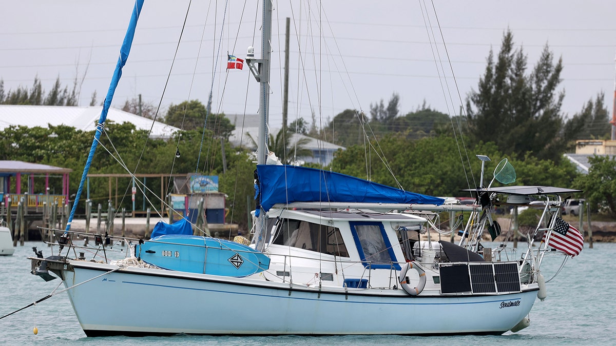 Soulmate boat anchored in calm turquoise water near a shoreline with lush green trees.