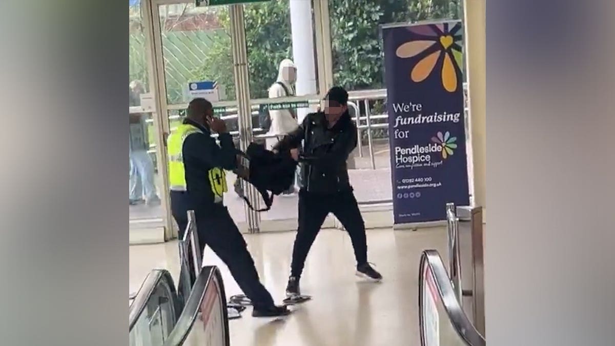 Two men stand across from each other, both grabbing and tugging at a single backpack between them.