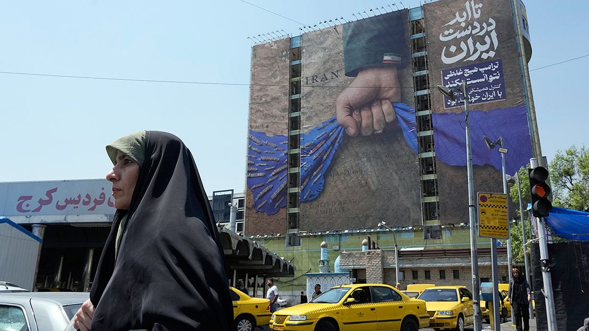 A woman walking past a billboard showing a military hand holding the Strait of Hormuz in Tehran
