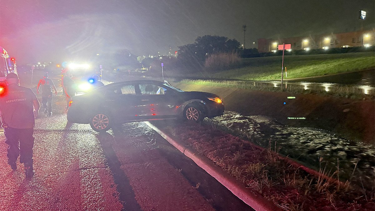 Police officer stands near partially submerged car in floodwaters in White Settlement, Texas at night