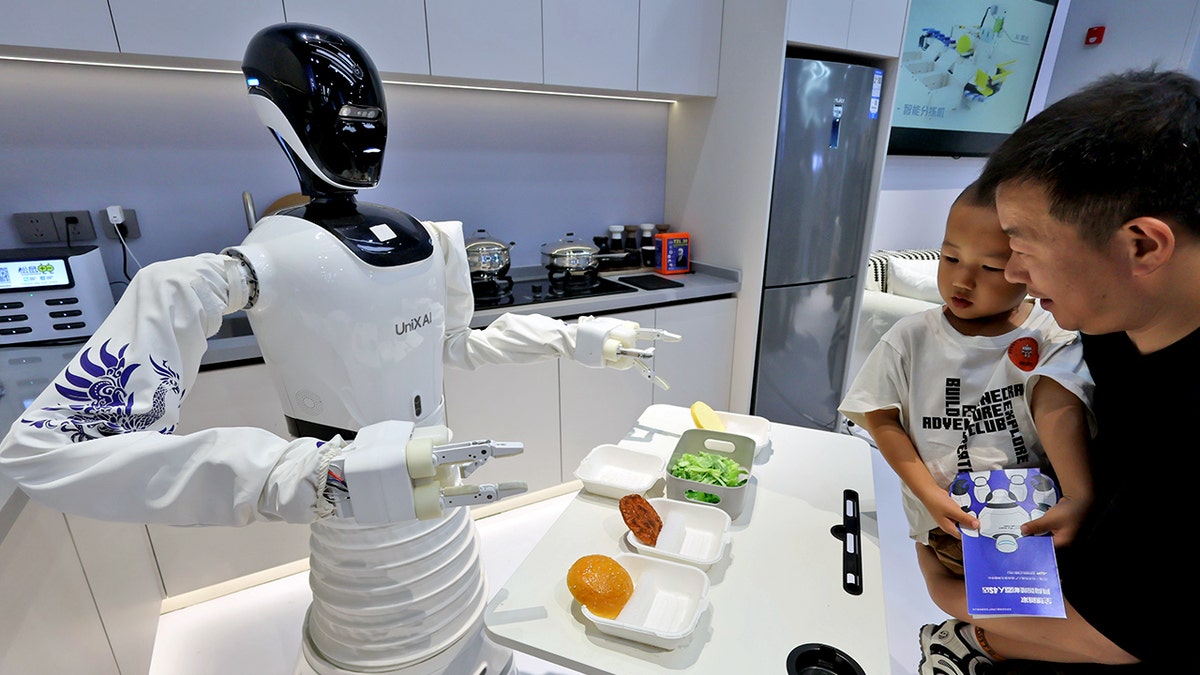 People look on at a robot presenting food in a kitchen.