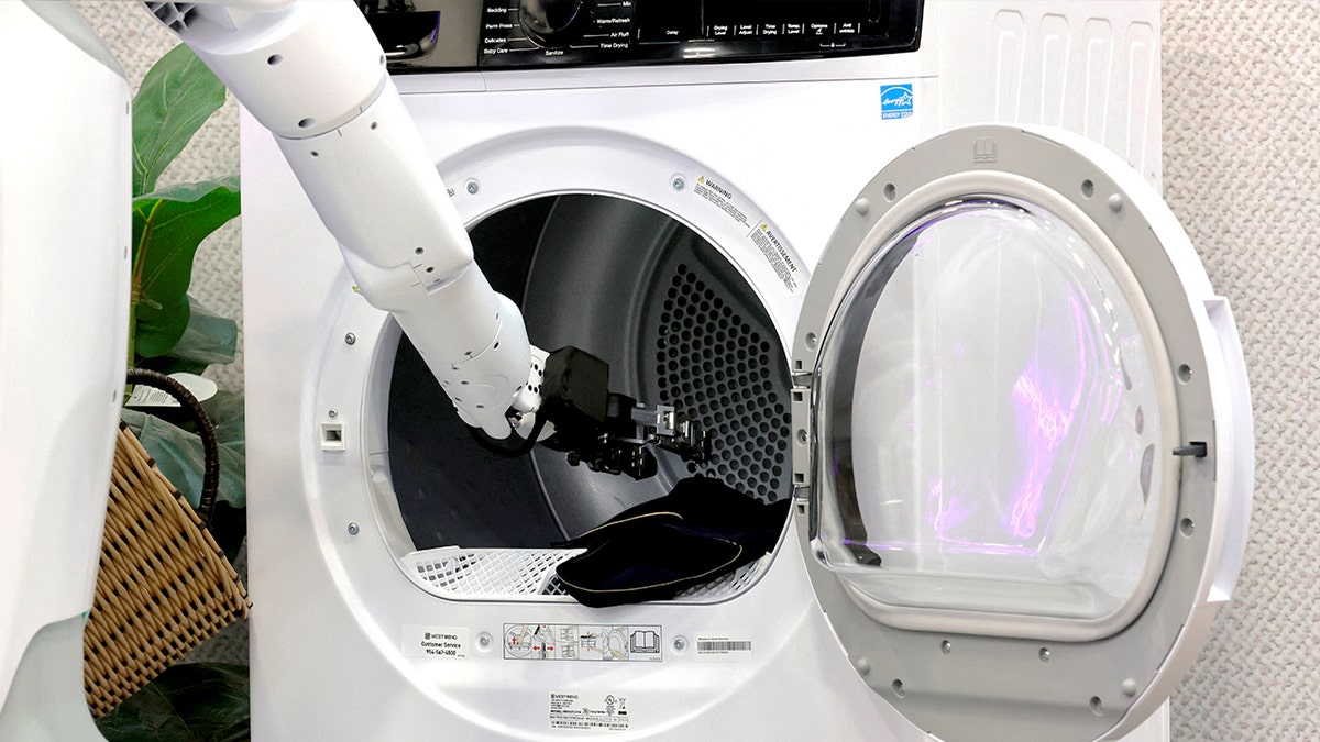 A robot arm loads a washing machine.